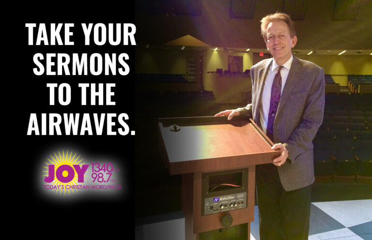 Man in a suit at a wooden pulpit on stage, with a promotional slogan: 'Take Your Sermons to the Airwaves' beside the JOY radio logo.